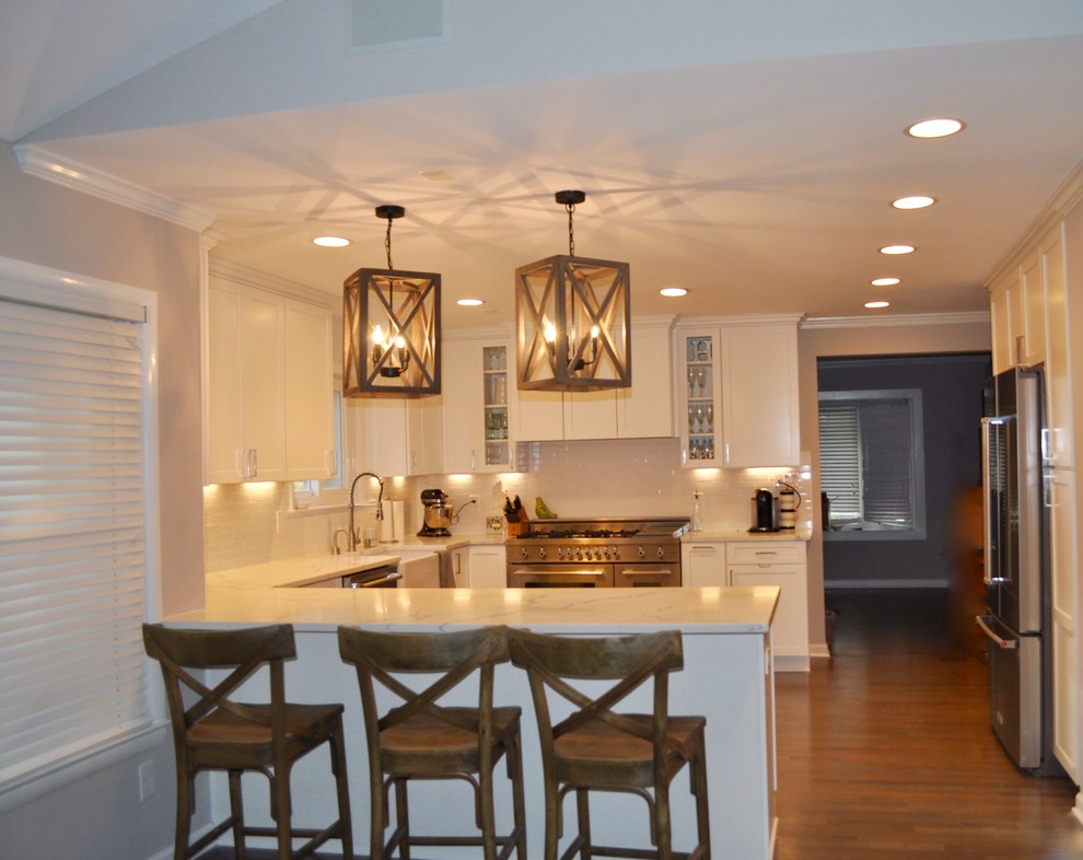 Inspiration for a mid-sized transitional u-shaped dark wood floor and brown floor kitchen remodel in DC Metro with a farmhouse sink, shaker cabinets, white cabinets, marble countertops, white backsplash, subway tile backsplash, stainless steel appliances and a peninsula