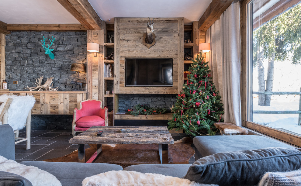 Inspiration for a mid-sized country open concept living room in Grenoble with a standard fireplace, a wood fireplace surround, a wall-mounted tv, grey floor, a library and slate floors.