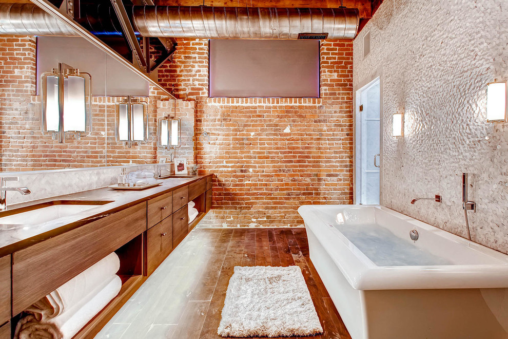 This is an example of a large contemporary master bathroom in Denver with an undermount sink, flat-panel cabinets, medium wood cabinets, wood benchtops, a freestanding tub, a shower/bathtub combo, a two-piece toilet, white tile, glass tile, orange walls and medium hardwood floors.
