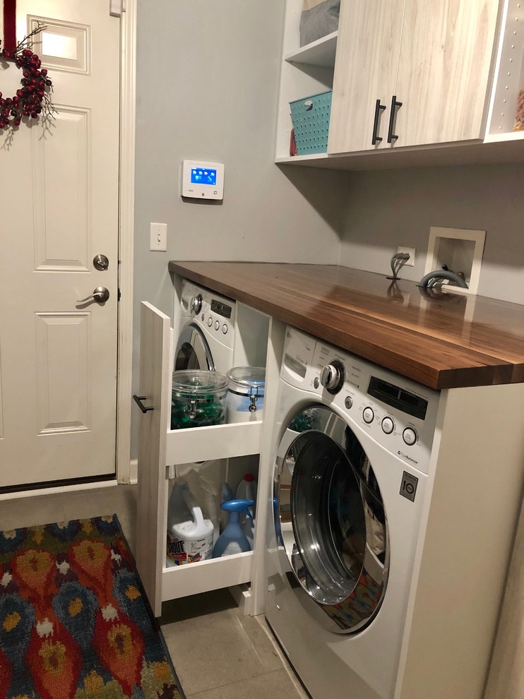 Photo of a mid-sized transitional galley utility room in Chicago with an utility sink, flat-panel cabinets, light wood cabinets, grey walls, porcelain floors, a side-by-side washer and dryer, grey floor and brown benchtop.