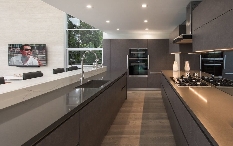 Large modern single-wall separate kitchen in Hawaii with an undermount sink, flat-panel cabinets, brown cabinets, solid surface benchtops, mirror splashback, black appliances, medium hardwood floors, with island, brown floor and brown benchtop.