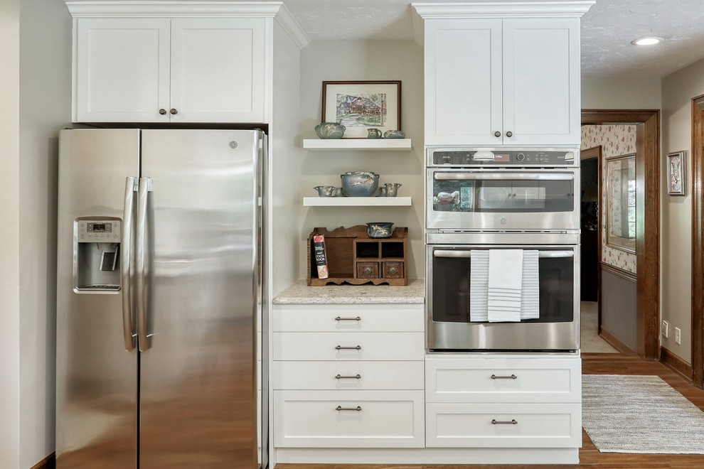 Example of a transitional vinyl floor and brown floor kitchen design with an undermount sink, white cabinets, quartz countertops, white backsplash, subway tile backsplash, stainless steel appliances, an island and beige countertops
