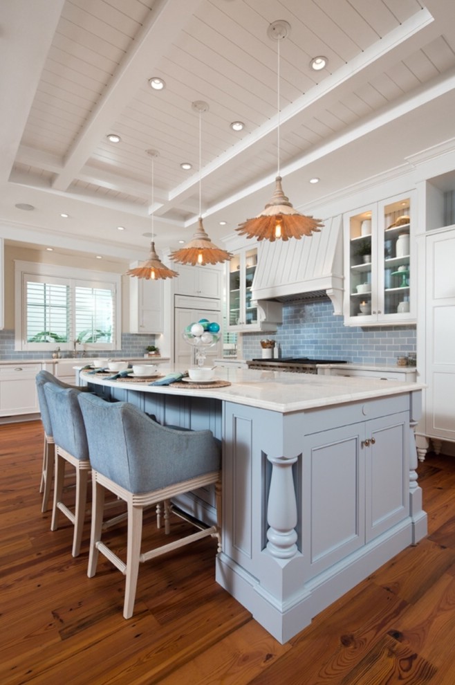 This is an example of a beach style kitchen in Miami with a farmhouse sink, white cabinets, blue splashback, subway tile splashback, medium hardwood floors, with island, white benchtop, panelled appliances and shaker cabinets.
