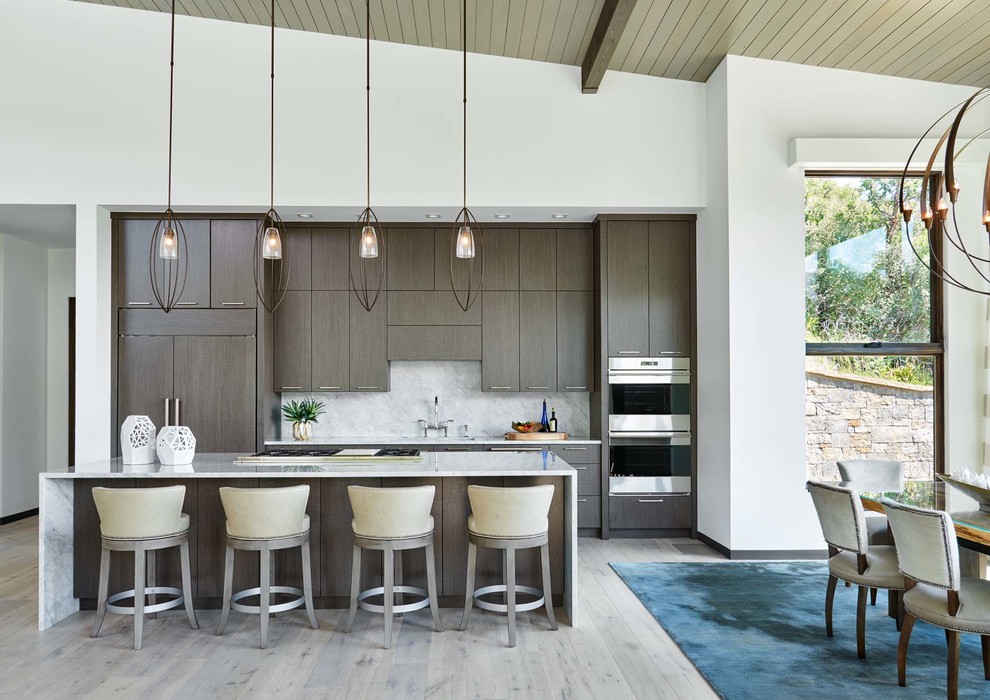 Design ideas for a mid-sized contemporary galley open plan kitchen in Denver with flat-panel cabinets, dark wood cabinets, white splashback, stone slab splashback, light hardwood floors, with island, grey floor, white benchtop, an undermount sink, marble benchtops and stainless steel appliances.