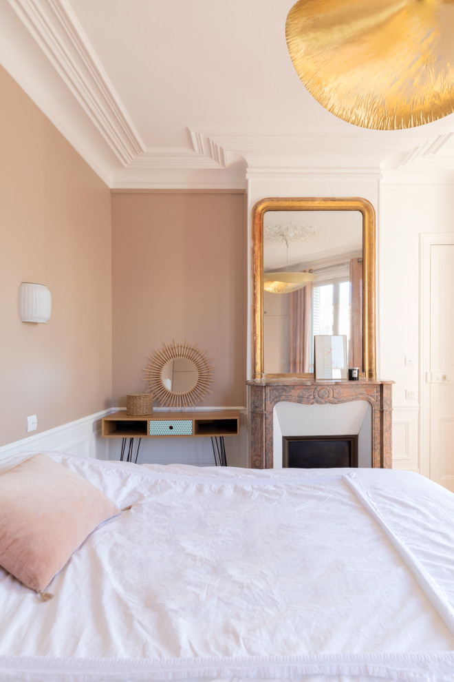Modelo de dormitorio principal moderno de tamaño medio con paredes rosas, suelo de madera en tonos medios, todas las chimeneas, marco de chimenea de piedra y suelo marrón