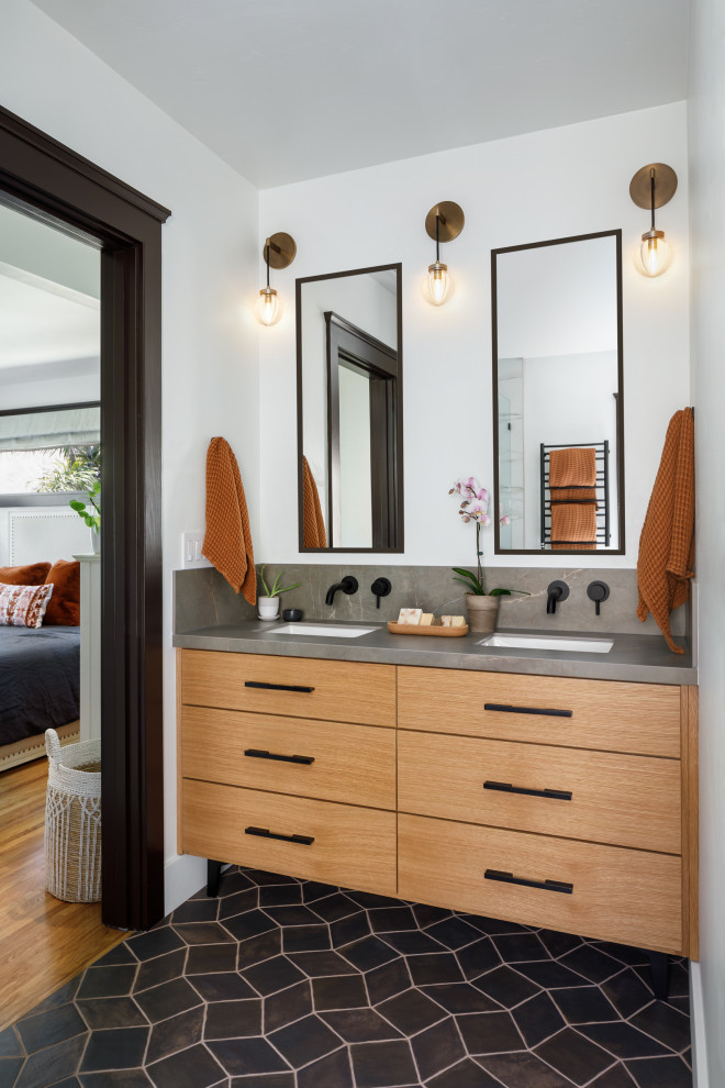 Photo of a mid-sized mediterranean master bathroom in San Diego with flat-panel cabinets, medium wood cabinets, a freestanding tub, an alcove shower, a one-piece toilet, white tile, porcelain tile, white walls, porcelain floors, an undermount sink, engineered quartz benchtops, black floor, a hinged shower door, grey benchtops, a niche, a double vanity and a built-in vanity.