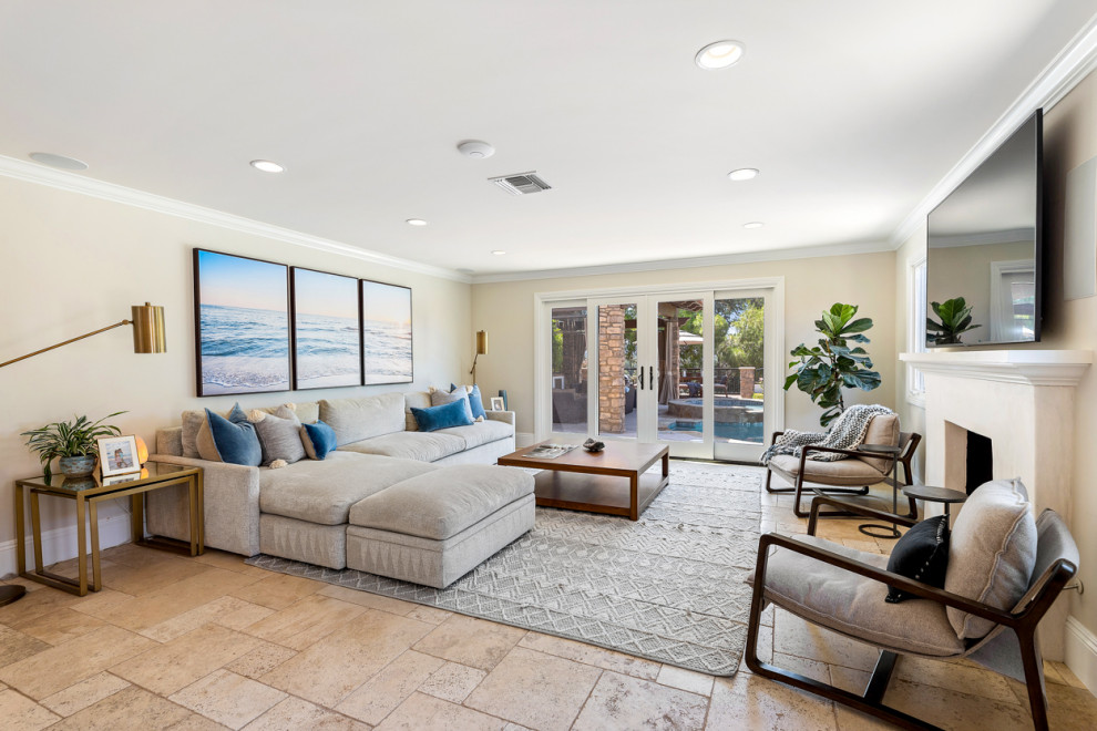 This is an example of a large mediterranean open concept family room in Los Angeles with beige walls, ceramic floors, a standard fireplace, a wall-mounted tv and beige floor.