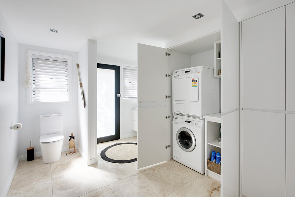 Photo of a mid-sized beach style galley utility room in Sydney with a single-bowl sink, flat-panel cabinets, white cabinets, quartz benchtops, multi-coloured splashback, engineered quartz splashback, white walls, travertine floors, a concealed washer and dryer, multi-coloured floor, multi-coloured benchtop, coffered and panelled walls.