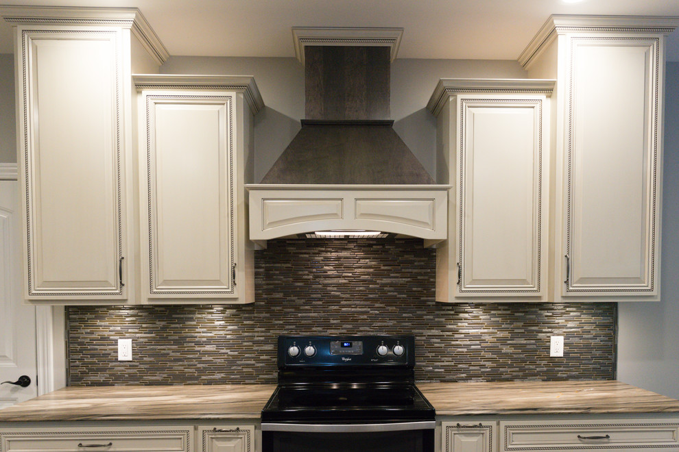 Large transitional l-shaped ceramic tile eat-in kitchen photo in Chicago with an undermount sink, raised-panel cabinets, dark wood cabinets, marble countertops, brown backsplash, glass tile backsplash, black appliances and an island