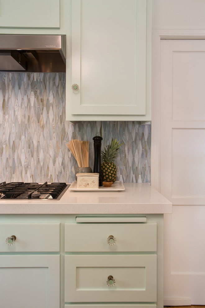 Inspiration for a mid-sized beach style l-shaped separate kitchen in Los Angeles with a peninsula, shaker cabinets, green cabinets, solid surface benchtops, green splashback, glass sheet splashback, stainless steel appliances, a single-bowl sink and medium hardwood floors.