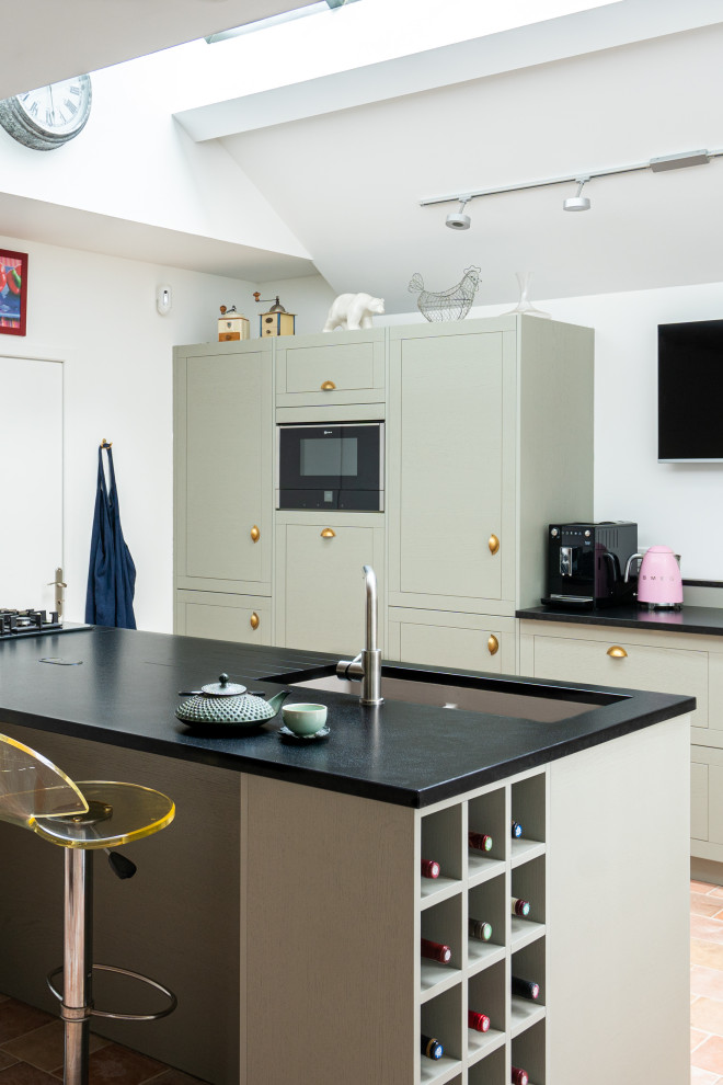 Expansive midcentury galley open plan kitchen in Other with an integrated sink, flat-panel cabinets, green cabinets, granite benchtops, black splashback, granite splashback, panelled appliances, cement tiles, with island, pink floor and black benchtop.
