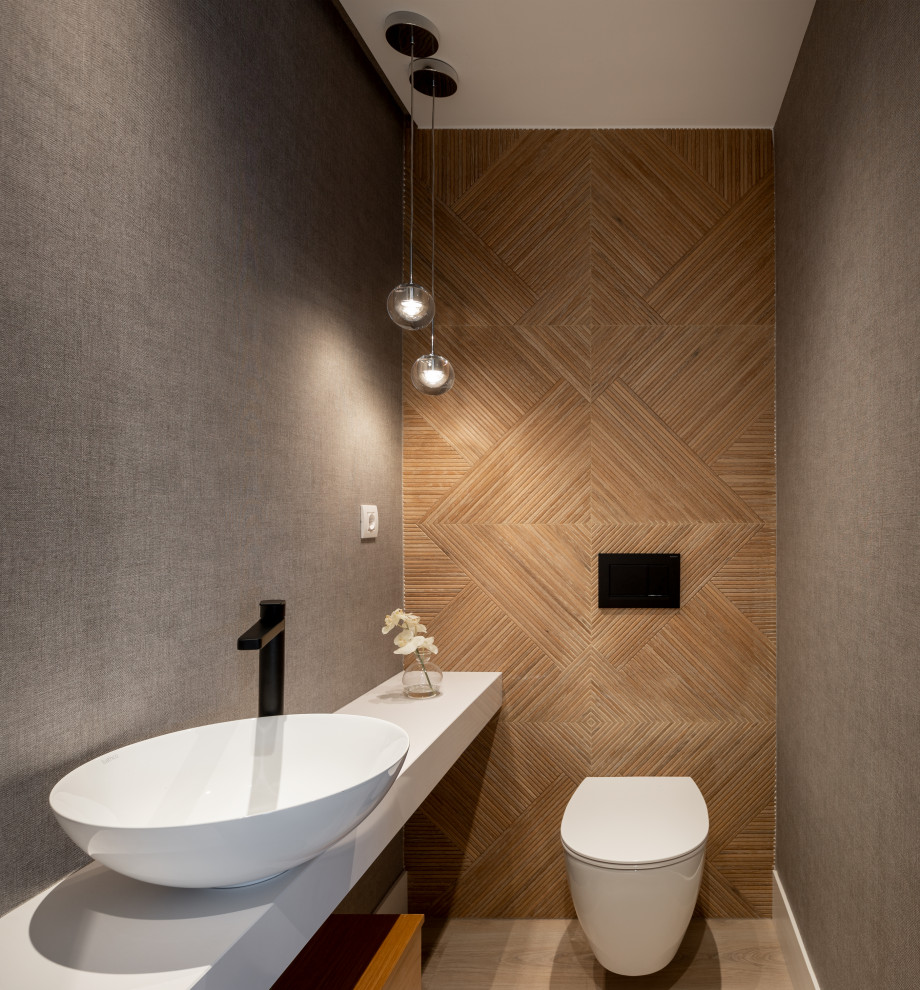 Modern inredning av ett mellanstort vit vitt toalett, med vita skåp, en vägghängd toalettstol, brun kakel, grå väggar, laminatgolv, ett fristående handfat, träbänkskiva och brunt golv