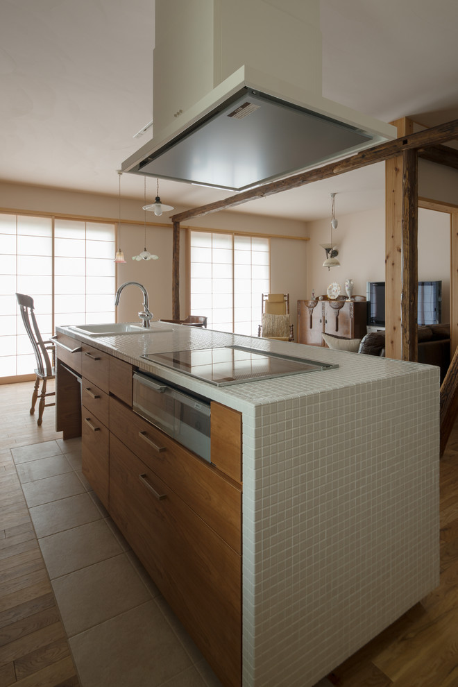 This is an example of a country single-wall open plan kitchen with a drop-in sink, beaded inset cabinets, medium wood cabinets, tile benchtops, porcelain floors, with island and beige floor.