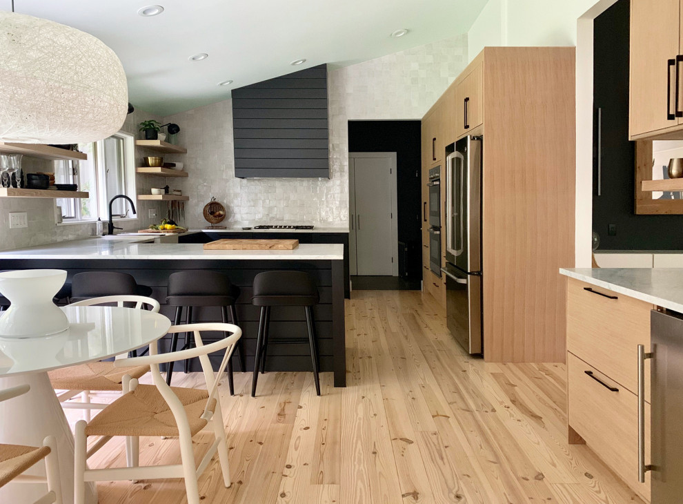 Photo of a large modern u-shaped eat-in kitchen in New York with a farmhouse sink, flat-panel cabinets, black cabinets, marble benchtops, white splashback, terra-cotta splashback, stainless steel appliances, light hardwood floors, beige floor and white benchtop.