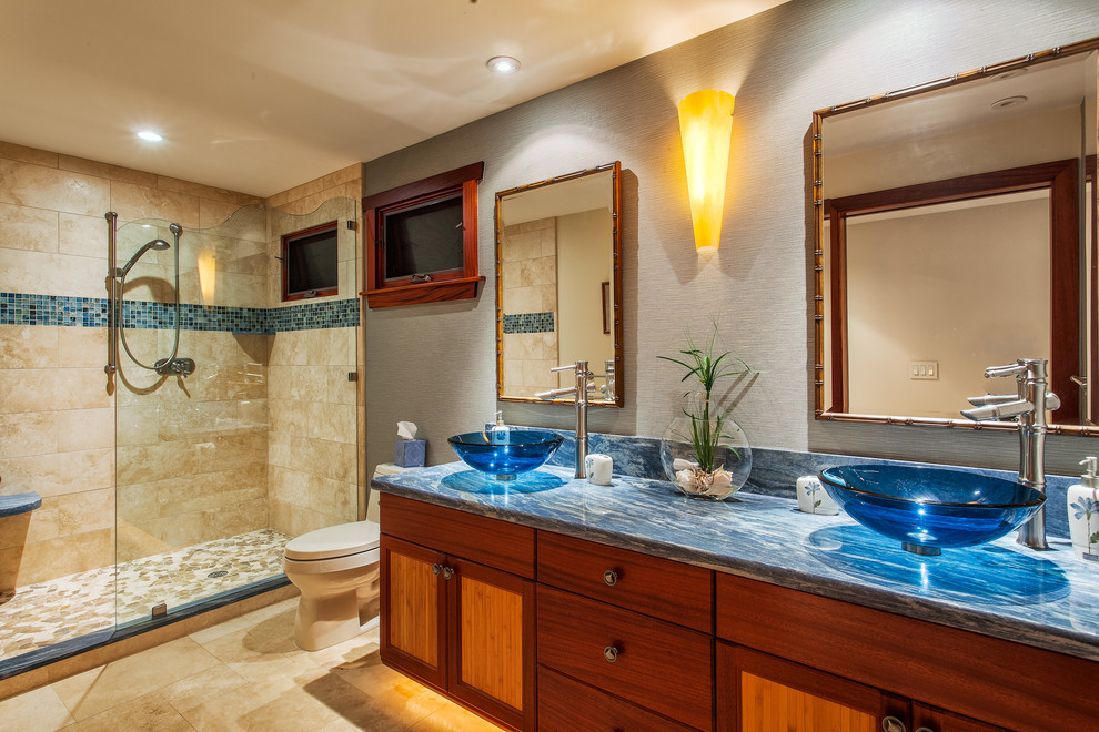 Inspiration for a large tropical 3/4 bathroom in Hawaii with a vessel sink, flat-panel cabinets, medium wood cabinets, granite benchtops, a corner shower, a one-piece toilet, beige tile, grey walls and travertine floors.