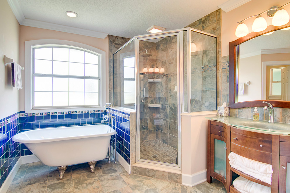 Photo of a traditional master bathroom in Jacksonville with furniture-like cabinets, medium wood cabinets, a claw-foot tub, a corner shower, multi-coloured tile, an integrated sink and glass benchtops.