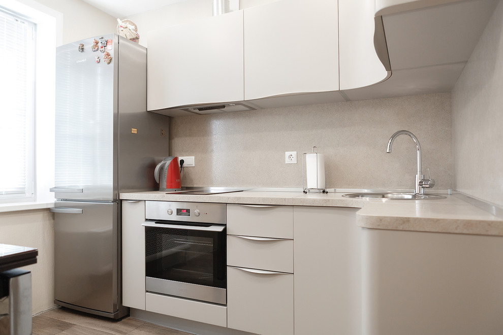 Inspiration for a small contemporary l-shaped kitchen in Moscow with an undermount sink, beige cabinets, granite benchtops, beige splashback, ceramic splashback, stainless steel appliances, laminate floors, with island, brown floor and beige benchtop.