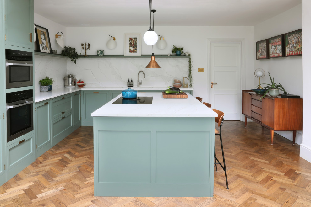 Example of a mid-sized transitional l-shaped medium tone wood floor and brown floor eat-in kitchen design in London with an integrated sink, shaker cabinets, green cabinets, quartzite countertops, white backsplash, quartz backsplash, stainless steel appliances, an island and white countertops
