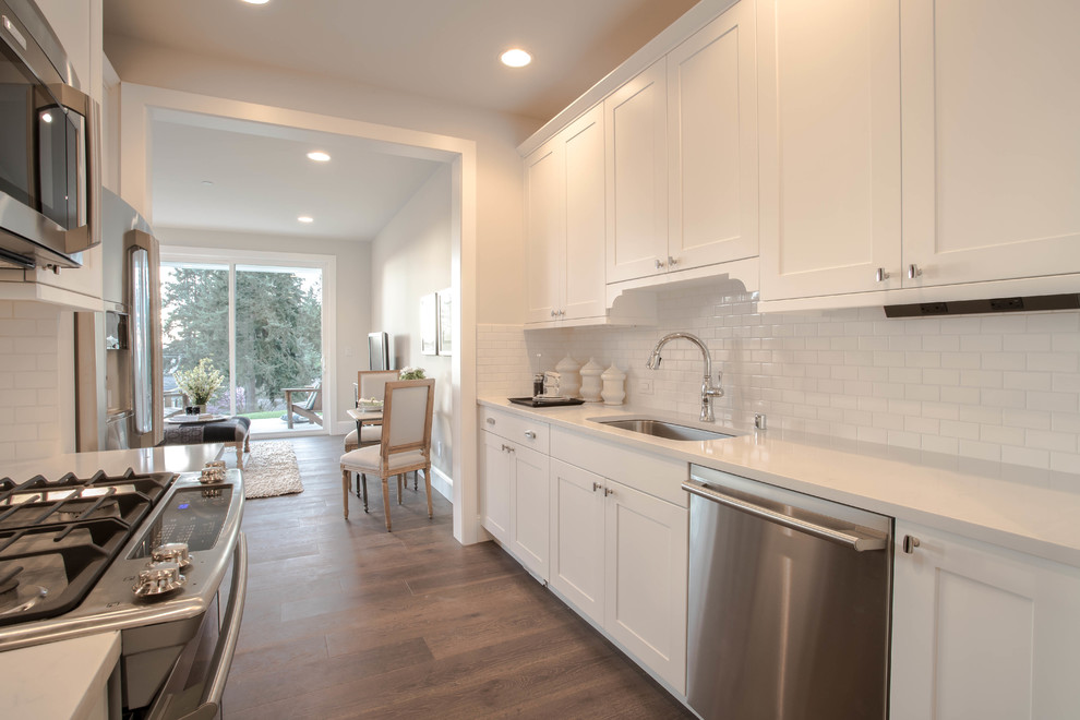 Example of a huge cottage l-shaped dark wood floor open concept kitchen design in Seattle with a farmhouse sink, shaker cabinets, white cabinets, marble countertops, white backsplash, stone tile backsplash, stainless steel appliances and an island