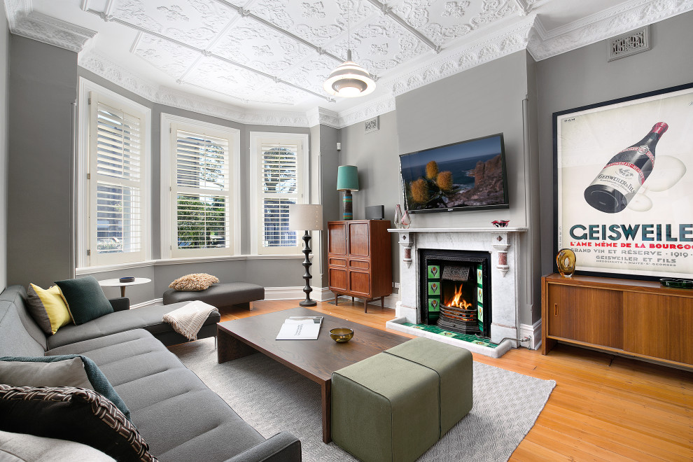 Photo of a transitional living room in Sydney with grey walls, medium hardwood floors, a standard fireplace and brown floor.