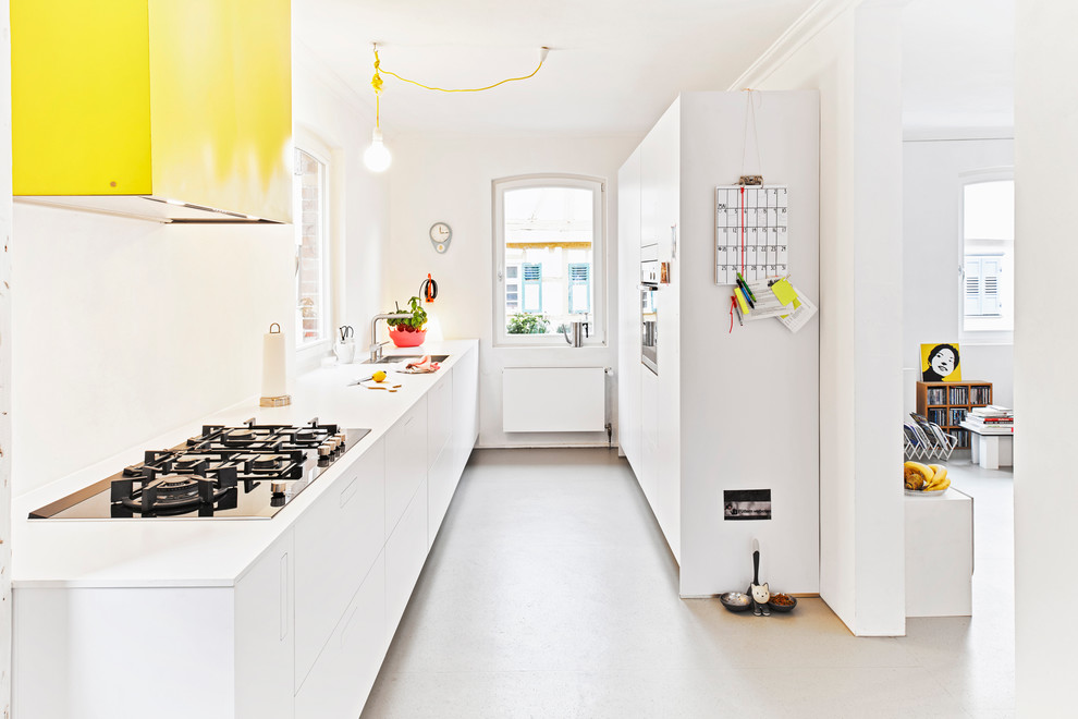 This is an example of a small contemporary galley open plan kitchen in Stuttgart with flat-panel cabinets, white cabinets, white splashback, concrete floors, no island, a drop-in sink and wood benchtops.