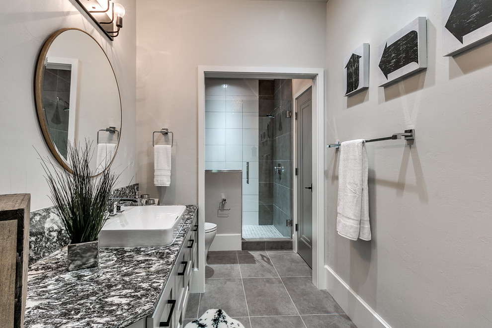 This is an example of a mid-sized transitional 3/4 bathroom in Oklahoma City with shaker cabinets, grey cabinets, an alcove shower, a one-piece toilet, black and white tile, porcelain tile, grey walls, porcelain floors, a vessel sink, marble benchtops, grey floor and a hinged shower door.