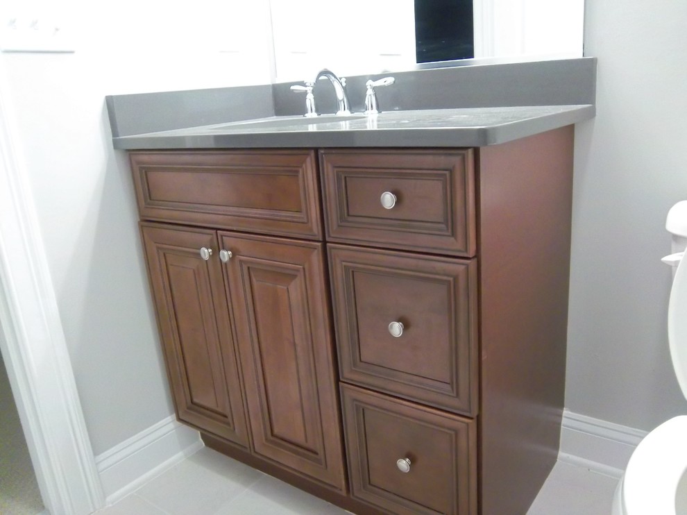 Example of a mid-sized transitional 3/4 bathroom design with raised-panel cabinets, dark wood cabinets, a two-piece toilet, gray walls, an undermount sink, solid surface countertops and gray countertops