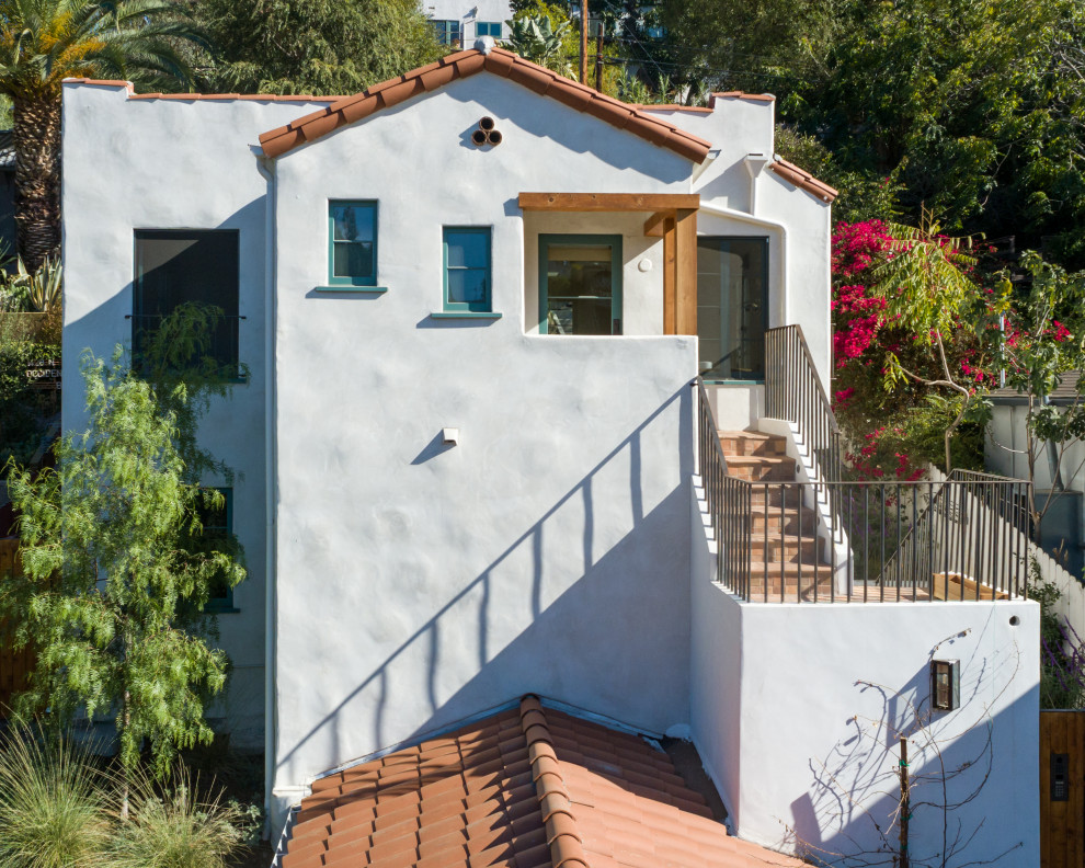 Modelo de fachada blanca mediterránea de tamaño medio de dos plantas con revestimiento de estuco y tejado de teja de barro