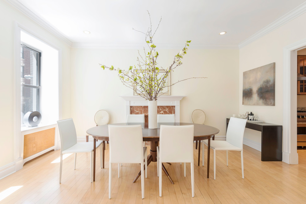 Mid-sized contemporary dining room in New York with beige walls, light hardwood floors and a standard fireplace.