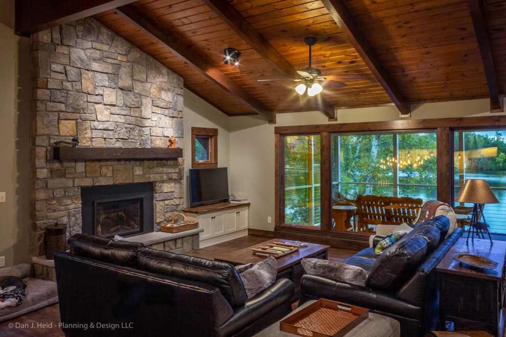 This is an example of a mid-sized country open concept living room in Minneapolis with beige walls, medium hardwood floors, a standard fireplace, a stone fireplace surround, a freestanding tv and brown floor.