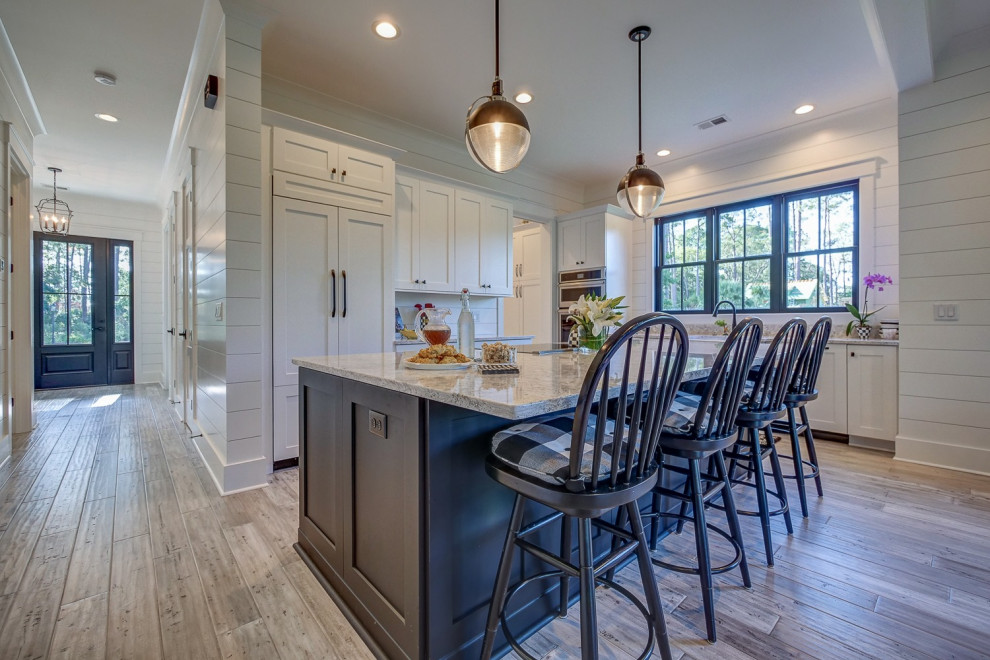 Open concept kitchen - mid-sized transitional l-shaped brown floor open concept kitchen idea with a farmhouse sink, shaker cabinets, white cabinets, quartz countertops, white backsplash, wood backsplash, stainless steel appliances, an island and multicolored countertops