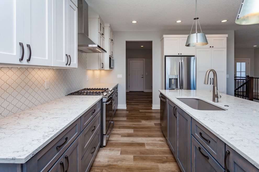Inspiration for a mid-sized transitional l-shaped light wood floor and brown floor open concept kitchen remodel with an undermount sink, shaker cabinets, white cabinets, quartz countertops, white backsplash, ceramic backsplash, stainless steel appliances, an island and white countertops