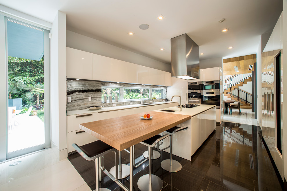 Photo of a contemporary l-shaped kitchen in Miami with flat-panel cabinets, white cabinets, grey splashback, stone slab splashback, stainless steel appliances and with island.