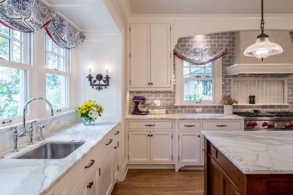 Design ideas for a large traditional kitchen in Minneapolis with an undermount sink, recessed-panel cabinets, white cabinets, marble benchtops, grey splashback, subway tile splashback, stainless steel appliances, medium hardwood floors and with island.