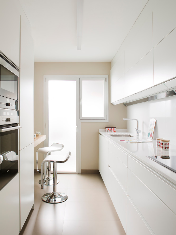 Mid-sized modern galley kitchen in Barcelona with stainless steel appliances, white splashback, an undermount sink, flat-panel cabinets, white cabinets, a peninsula, beige floor and white benchtop.