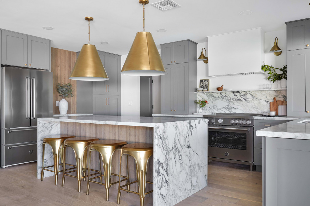 Transitional u-shaped kitchen in Phoenix with an undermount sink, shaker cabinets, grey cabinets, white splashback, stone slab splashback, stainless steel appliances, medium hardwood floors, with island, brown floor and white benchtop.