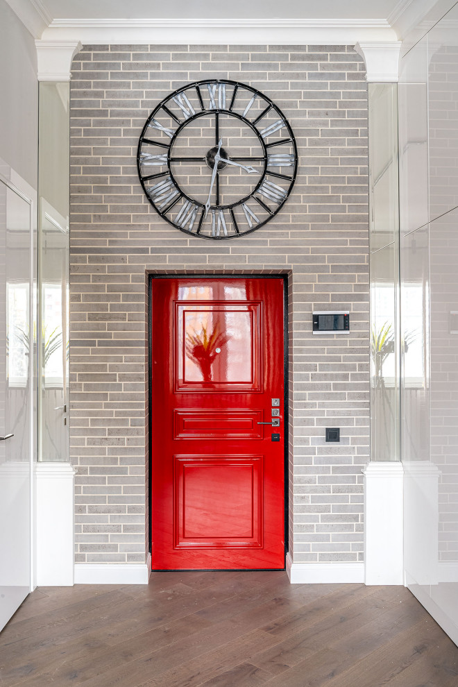 На фото: входная дверь в современном стиле с серыми стенами, паркетным полом среднего тона, одностворчатой входной дверью, красной входной дверью и кирпичными стенами с