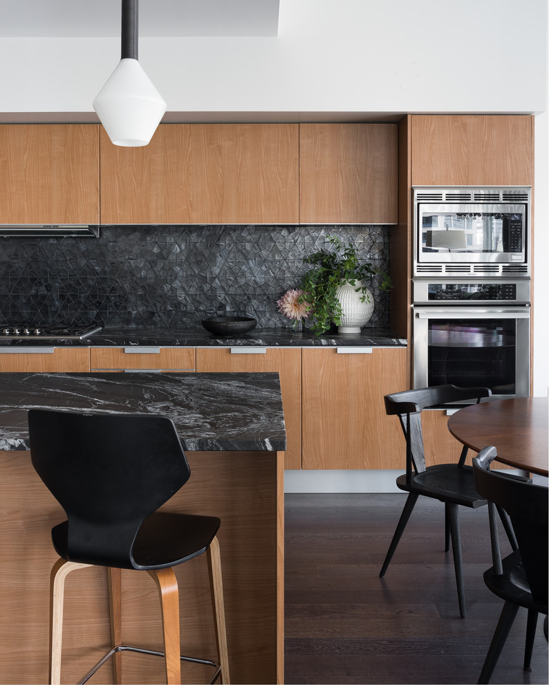 This is an example of a contemporary galley eat-in kitchen in Seattle with flat-panel cabinets, medium wood cabinets, black splashback, stone slab splashback, stainless steel appliances, dark hardwood floors, with island, brown floor and black benchtop.