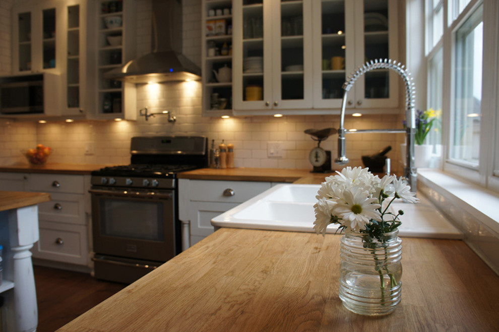 Open concept kitchen - large transitional u-shaped medium tone wood floor open concept kitchen idea in Ottawa with a farmhouse sink, shaker cabinets, distressed cabinets, wood countertops, white backsplash, subway tile backsplash, stainless steel appliances and an island