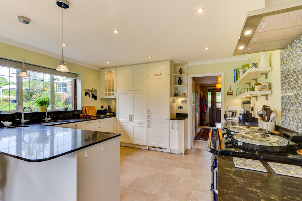 This is an example of a medium sized country cream and black u-shaped open plan kitchen in Sussex with a submerged sink, shaker cabinets, beige cabinets, quartz worktops, blue splashback, mosaic tiled splashback, integrated appliances, vinyl flooring, an island, beige floors, black worktops, all types of ceiling and feature lighting.