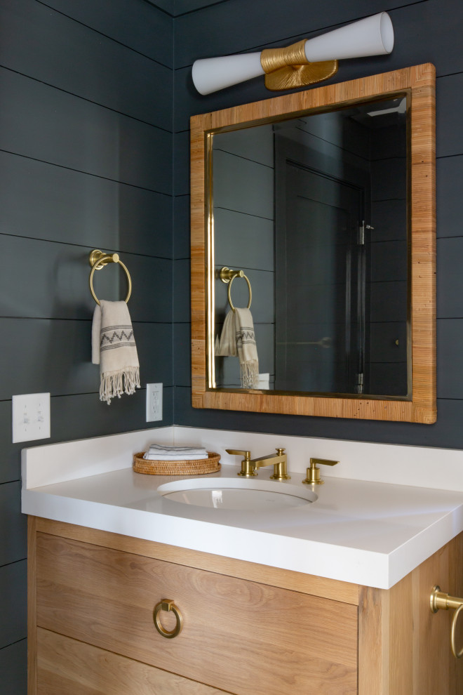 Photo of a mid-sized beach style powder room in Boston with flat-panel cabinets, light wood cabinets, an undermount sink, engineered quartz benchtops, white benchtops and black walls.