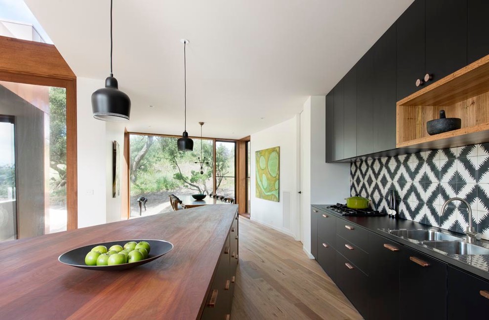Photo of a mid-sized contemporary eat-in kitchen in Melbourne with a double-bowl sink, flat-panel cabinets, wood benchtops, multi-coloured splashback, cement tile splashback, panelled appliances, medium hardwood floors and with island.