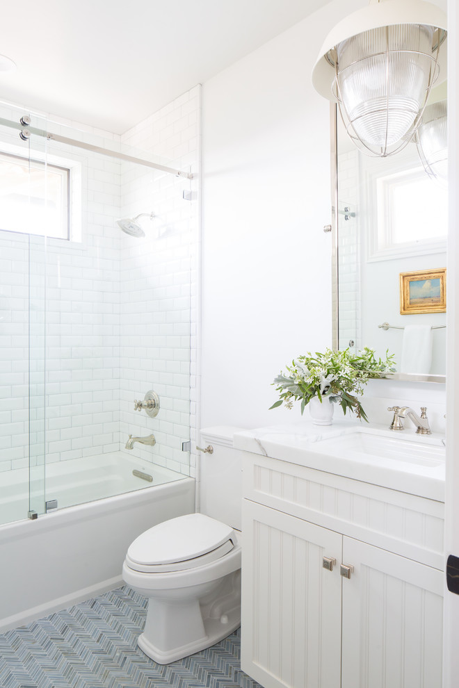 This is an example of a transitional bathroom in San Diego with white cabinets, white walls, ceramic floors, marble benchtops, blue floor, a sliding shower screen, an alcove tub, a shower/bathtub combo, an undermount sink, white benchtops and recessed-panel cabinets.
