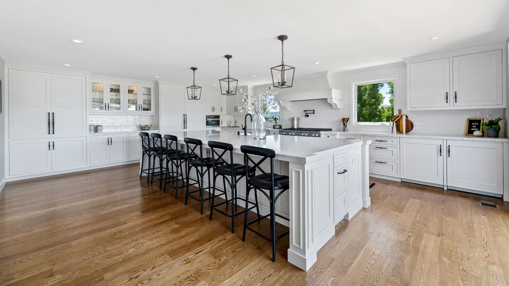 Eat-in kitchen - large transitional single-wall medium tone wood floor and brown floor eat-in kitchen idea with a single-bowl sink, raised-panel cabinets, white cabinets, quartzite countertops, white backsplash, ceramic backsplash, stainless steel appliances, an island and white countertops