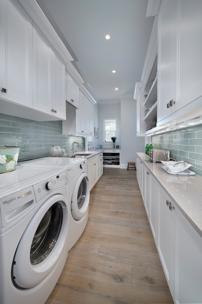 Photo of a mid-sized transitional galley utility room in Miami with an undermount sink, recessed-panel cabinets, white cabinets, quartz benchtops, grey walls, medium hardwood floors, a side-by-side washer and dryer, brown floor and grey benchtop.