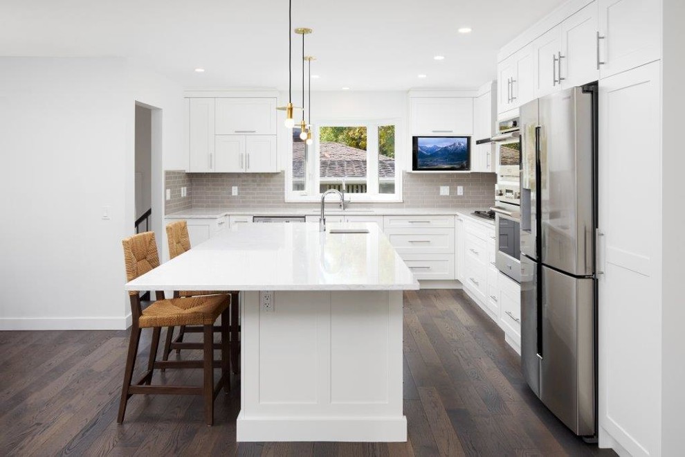 Mid-sized transitional l-shaped dark wood floor and brown floor open concept kitchen photo in Calgary with an undermount sink, shaker cabinets, white cabinets, quartz countertops, gray backsplash, subway tile backsplash, stainless steel appliances and an island