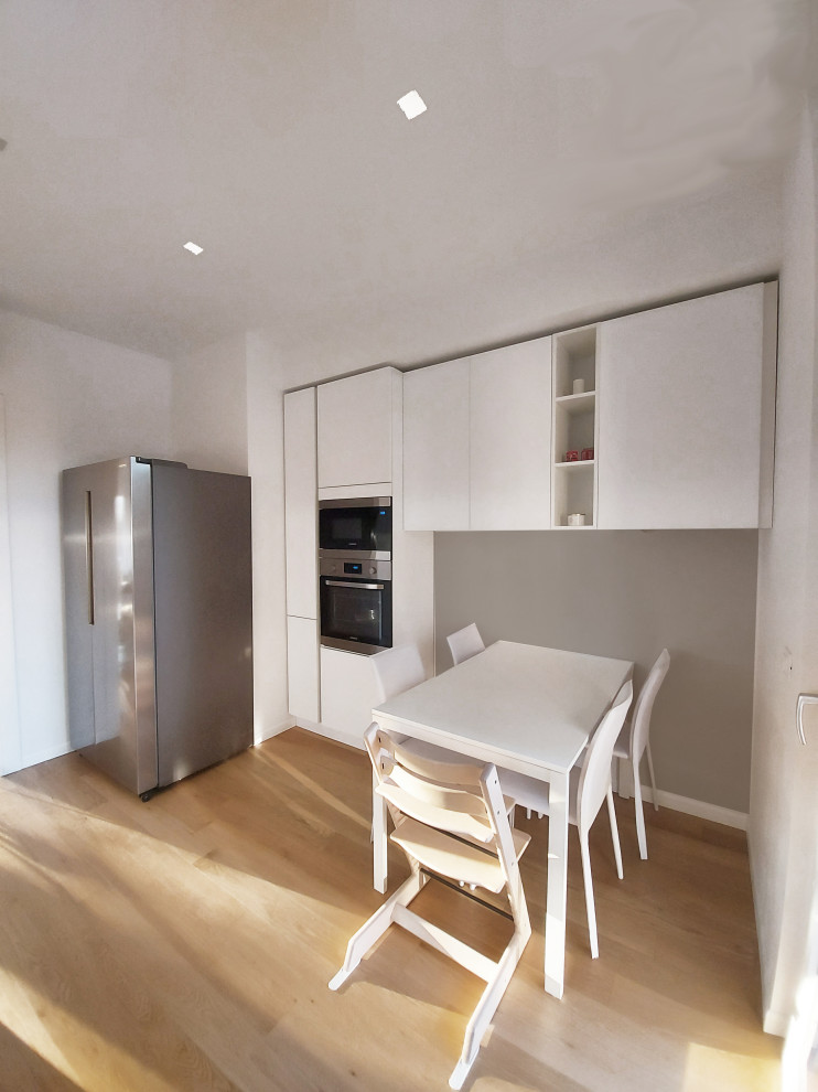 Medium sized contemporary galley enclosed kitchen in Milan with a built-in sink, flat-panel cabinets, white cabinets, quartz worktops, white splashback, porcelain splashback, light hardwood flooring, black worktops and a drop ceiling.