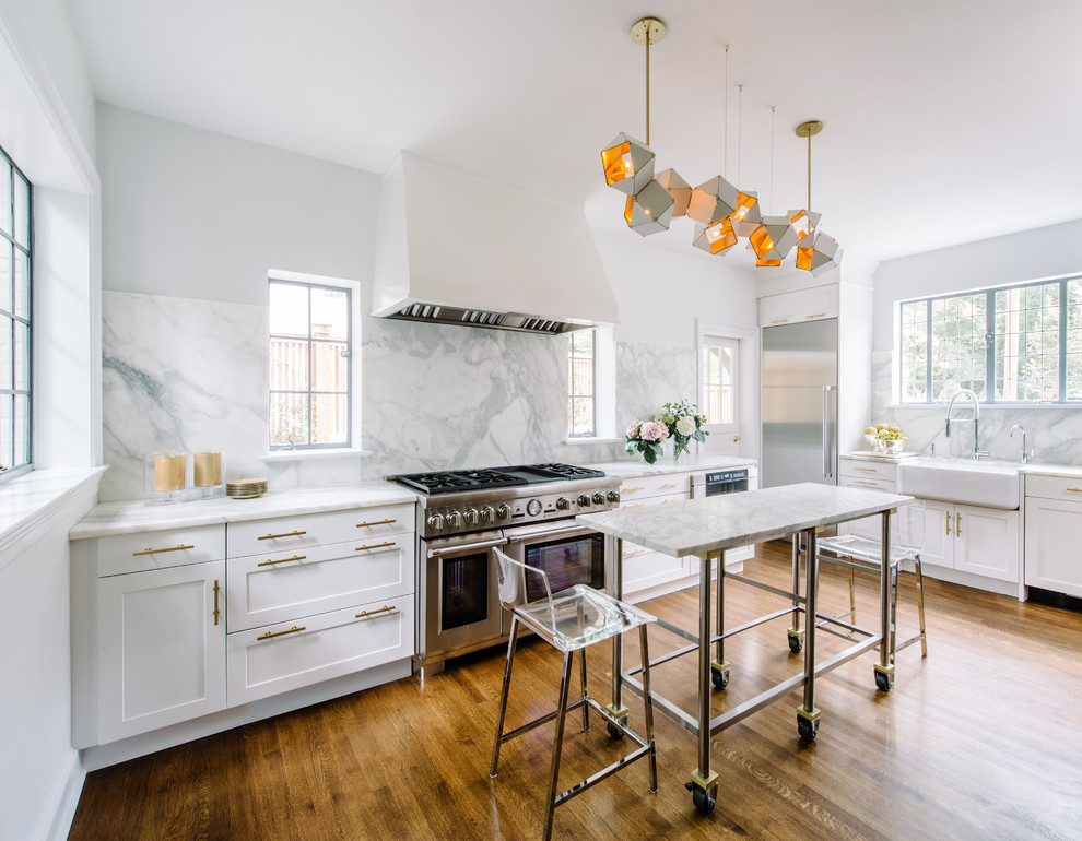 Design ideas for a large transitional l-shaped separate kitchen in DC Metro with a farmhouse sink, white cabinets, marble benchtops, white splashback, marble splashback, stainless steel appliances, medium hardwood floors, with island, brown floor and shaker cabinets.