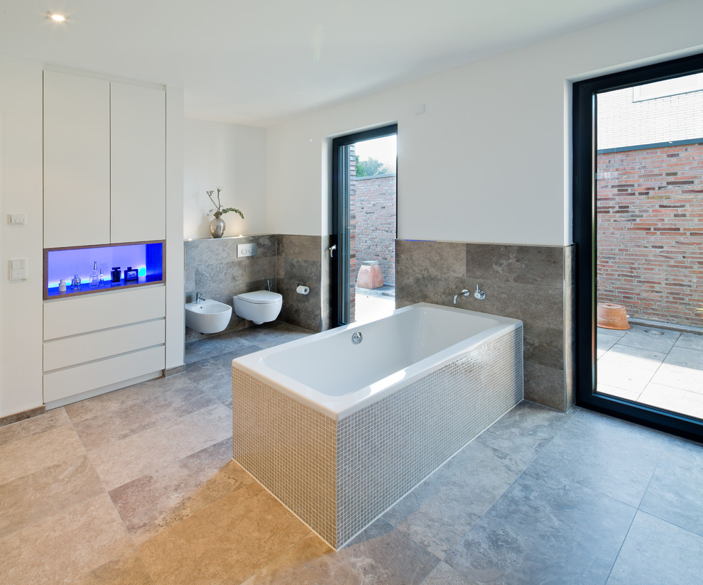 Photo of a large contemporary master bathroom in Dusseldorf with flat-panel cabinets, white cabinets, white walls, a drop-in tub, a bidet, brown tile and metal tile.