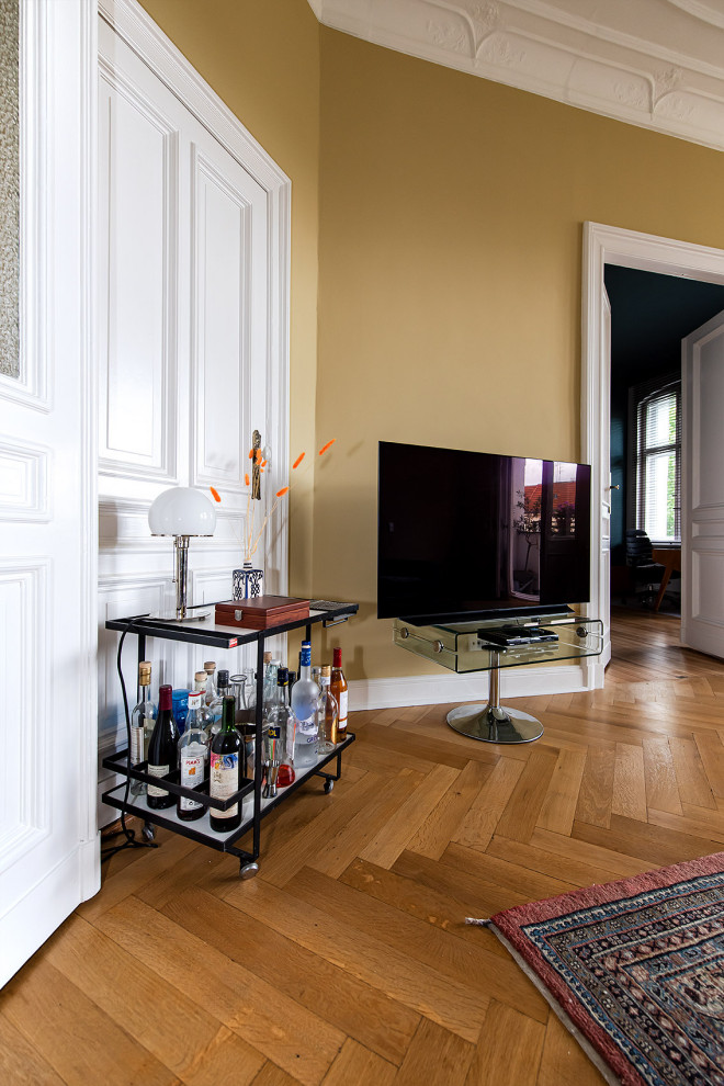 Пример оригинального дизайна: большая изолированная гостиная комната в стиле фьюжн с домашним баром, желтыми стенами, светлым паркетным полом, отдельно стоящим телевизором и коричневым полом